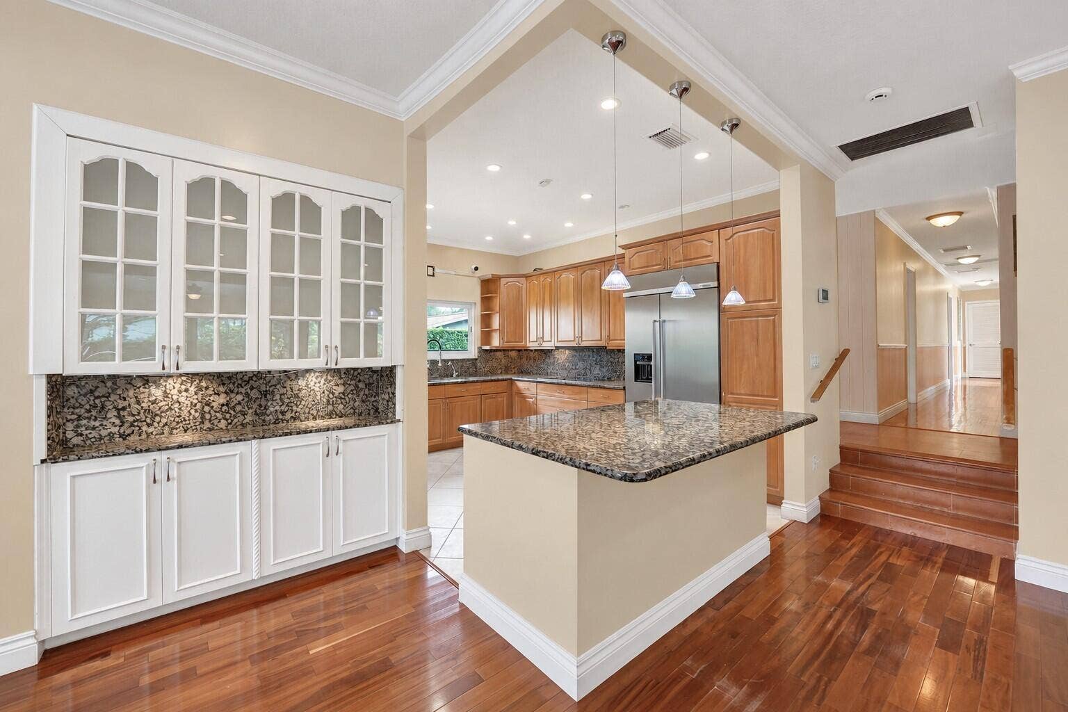 Wood flooring throughout, with a built-in white cabinetry unit featuring glass panel doors and under-cabinet lighting. Wall color has been virtually enhanced.