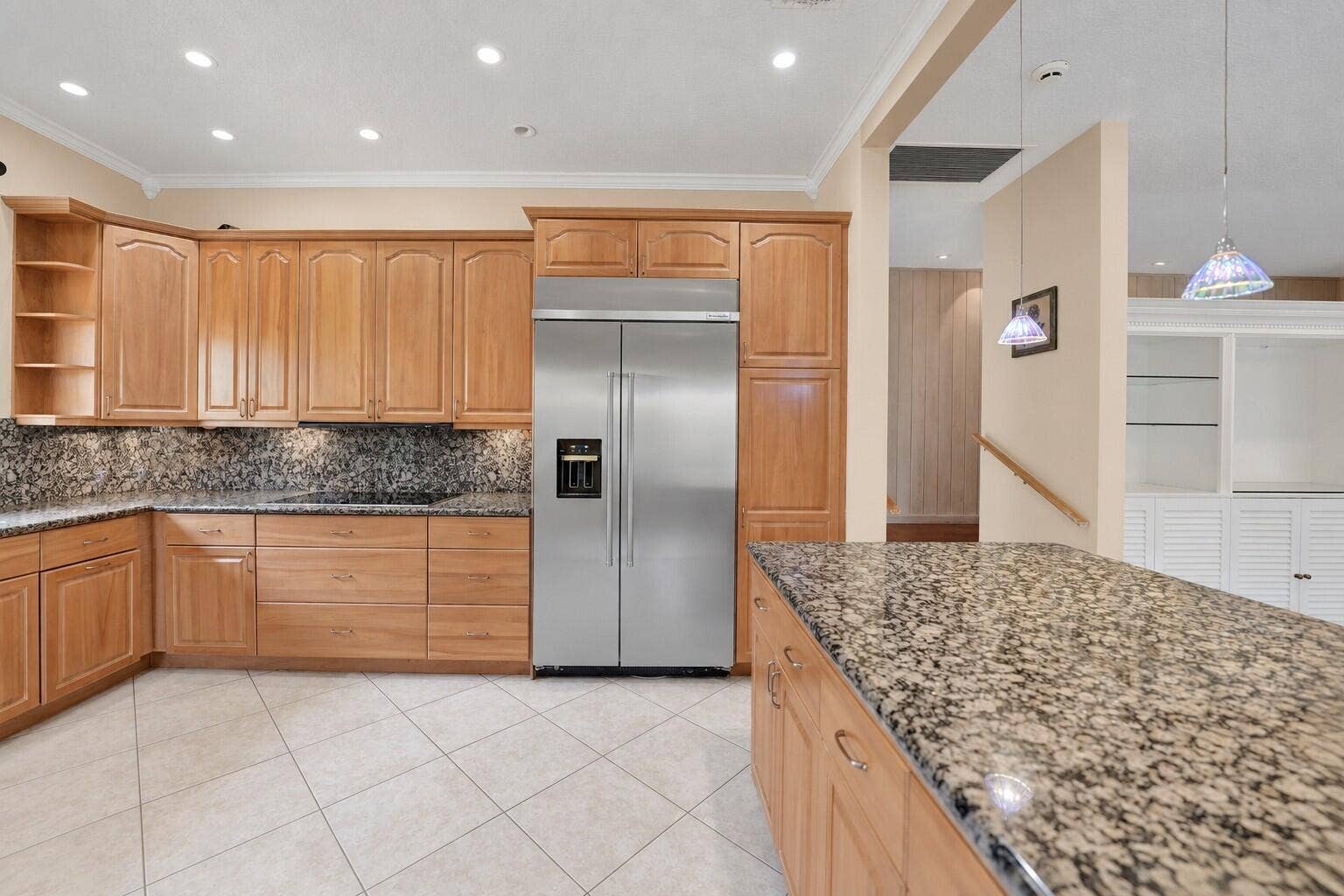 Kitchen featuring extensive wood cabinetry, stainless steel refrigerator, patterned stone countertops, recessed lighting, and tile flooring. Wall color has been virtually enhanced.