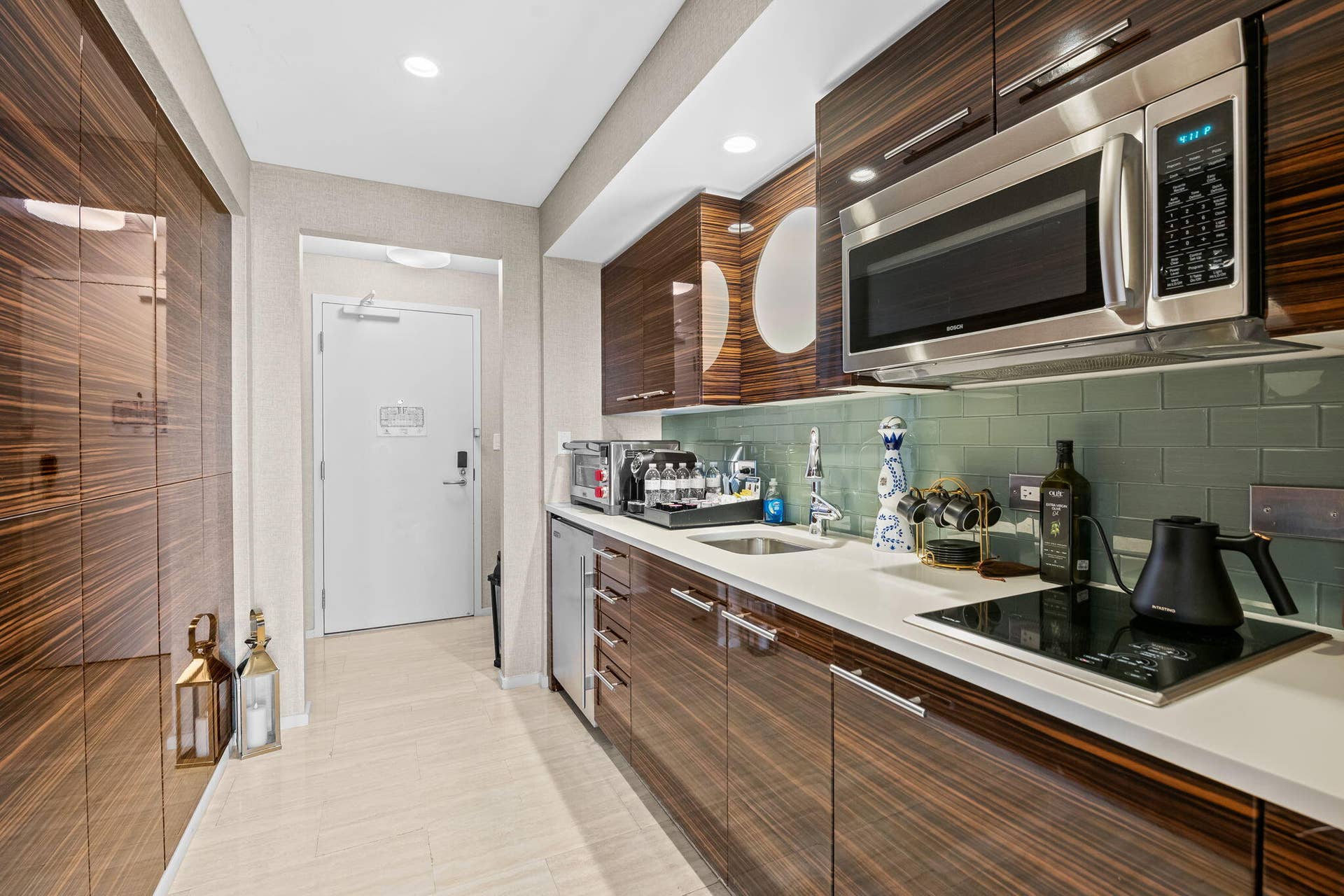 551 N FORT LAUDERDALE BEACH Boulevard, #R1801, Fort Lauderdale, FL 33304 Compact kitchen featuring wood-grain cabinetry, stainless steel microwave, light-colored countertops, tiled backsplash, and an integrated cooktop