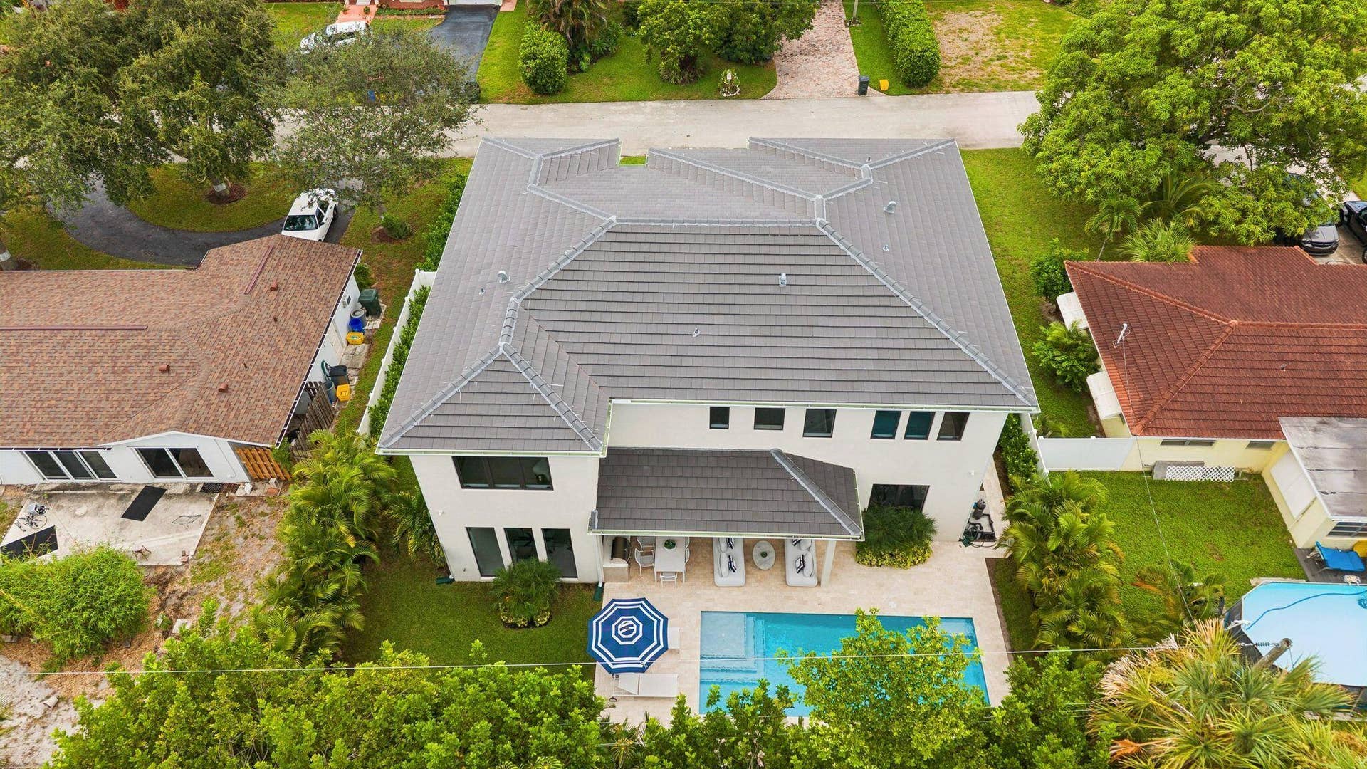 Exterior featuring a tiled roof, white stucco facade, multiple windows, an outdoor swimming pool, and surrounding green landscaping