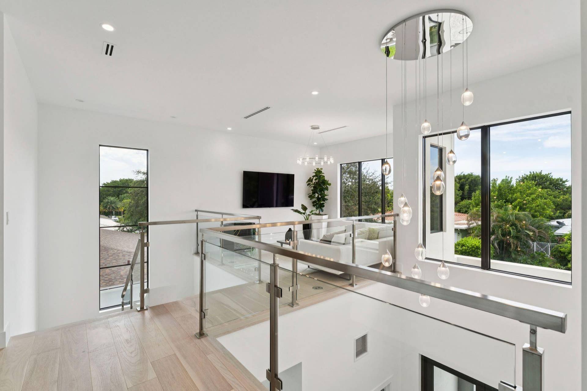 Light wood-finish flooring, glass and stainless steel railing, contemporary suspended lighting fixture, recessed ceiling lighting, and large windows