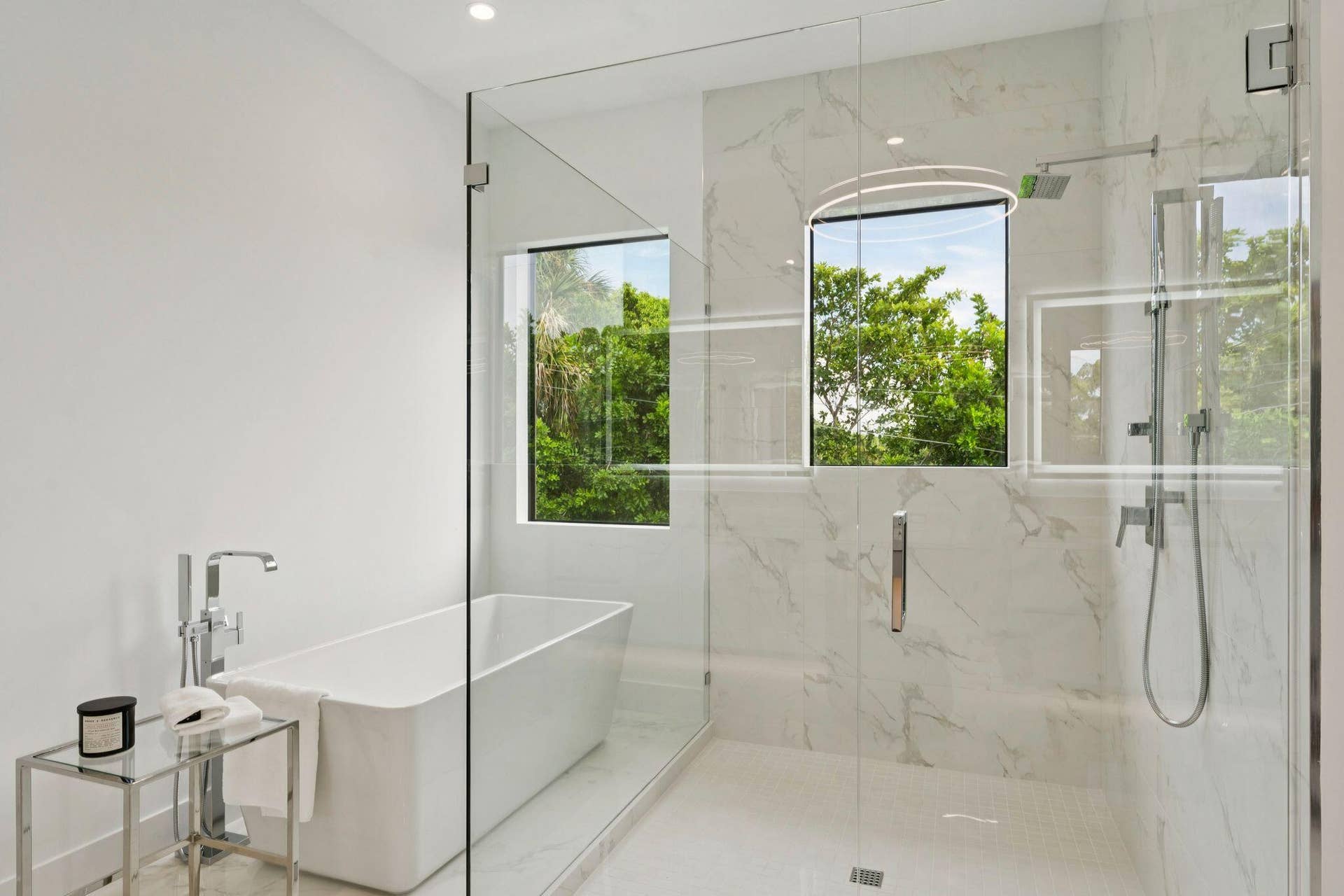 Freestanding soaking tub with a floor-mounted faucet, glass-enclosed shower, and large format wall tiling