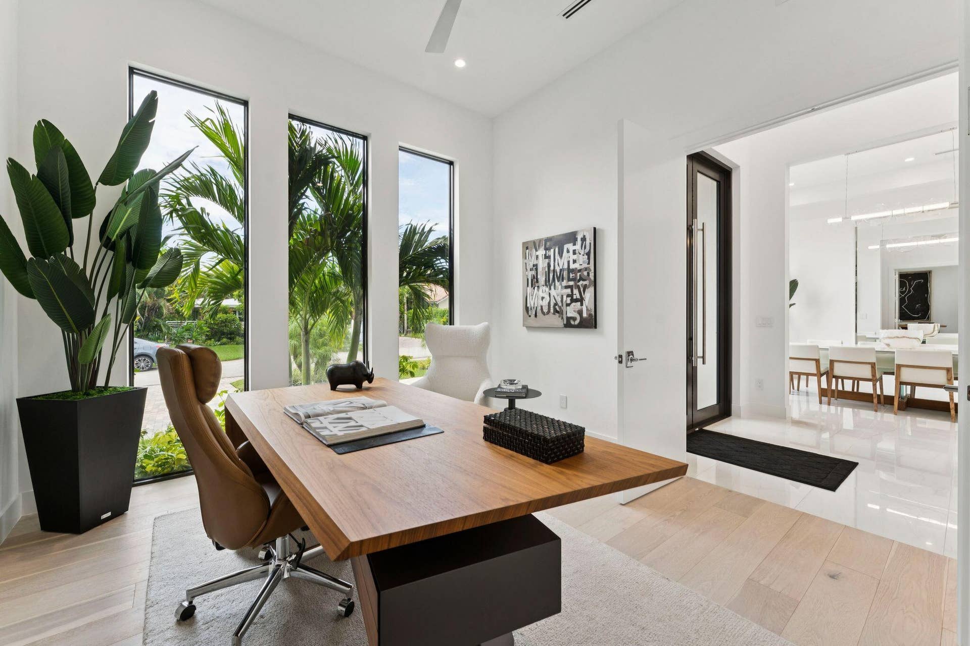 White walls with three tall windows, light wood-finish flooring, recessed lighting, and a modern glass entry door
