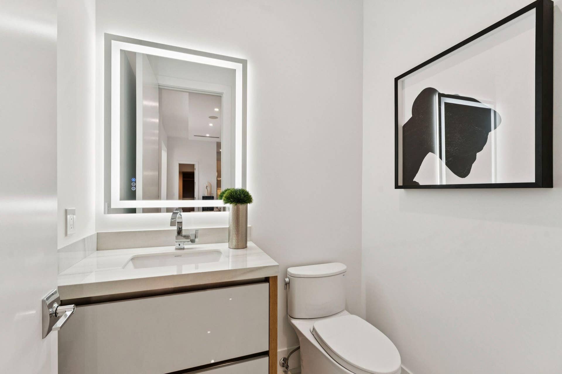 Modern vanity with an integrated sink, polished chrome faucet, illuminated mirror, and a contemporary toilet