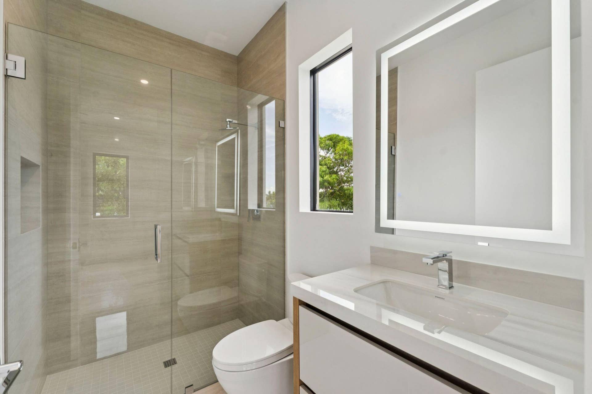 Glass-enclosed shower with integrated niche, modern vanity with an under-mount sink, sleek wall-mounted faucet, and an illuminated mirror