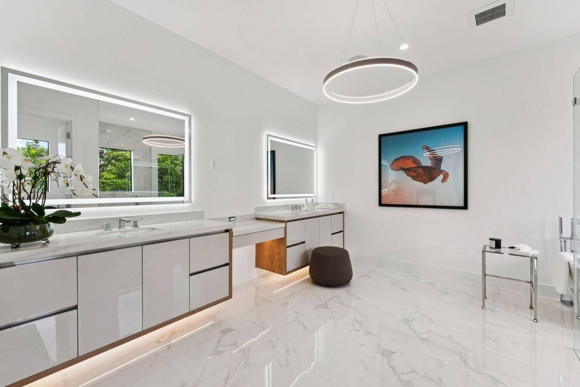 White marble-look flooring, dual vanity with undermount sinks and quartz countertops, back-lit mirrors, vanity lighting, and modern ring chandelier