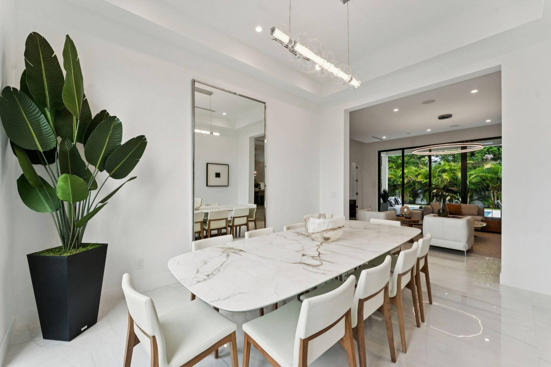 Open-concept dining area with a linear chandelier, large mirrored wall, and tile flooring