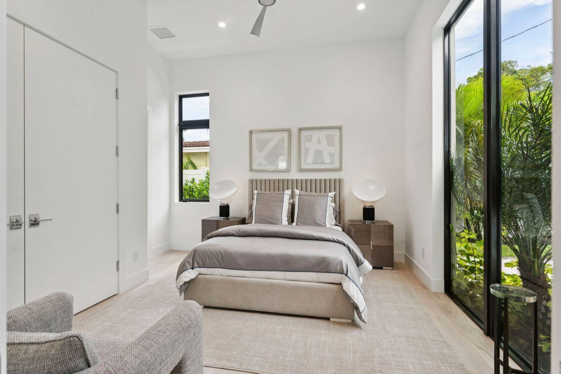 Light wood-finish flooring, full-height windows, a vertical slat headboard, recessed lighting, and a ceiling fan