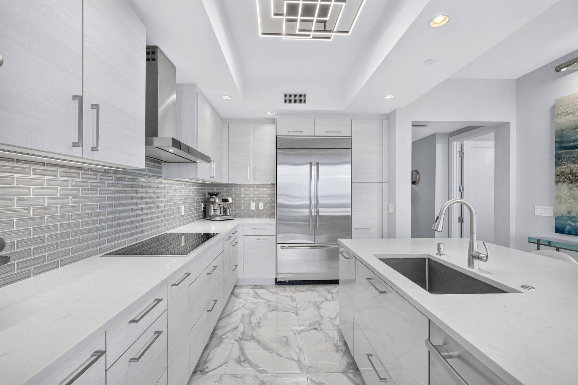 1 Water Club Way, #503, North Palm Beach, FL 33408 Large Open Concept Gourmet kitchen featuring a built-in cooktop, stainless steel High end appliances, a kitchen island with an undermount sink, a custom subway tile backsplash, and marble-finish flooring