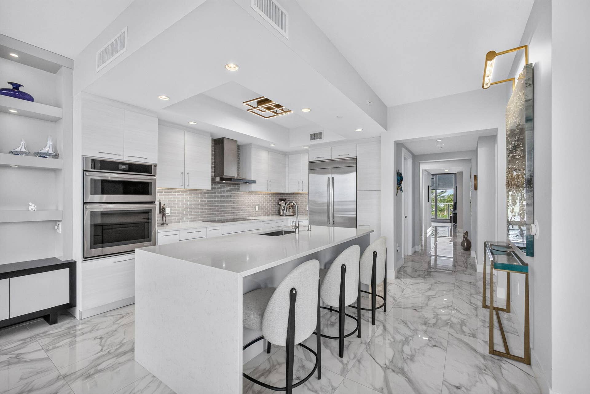 1 Water Club Way, #503, North Palm Beach, FL 33408 White shaker cabinetry, built-in stainless steel double ovens, large center island with counter seating, stainless steel appliances, and large format marble-look tile flooring