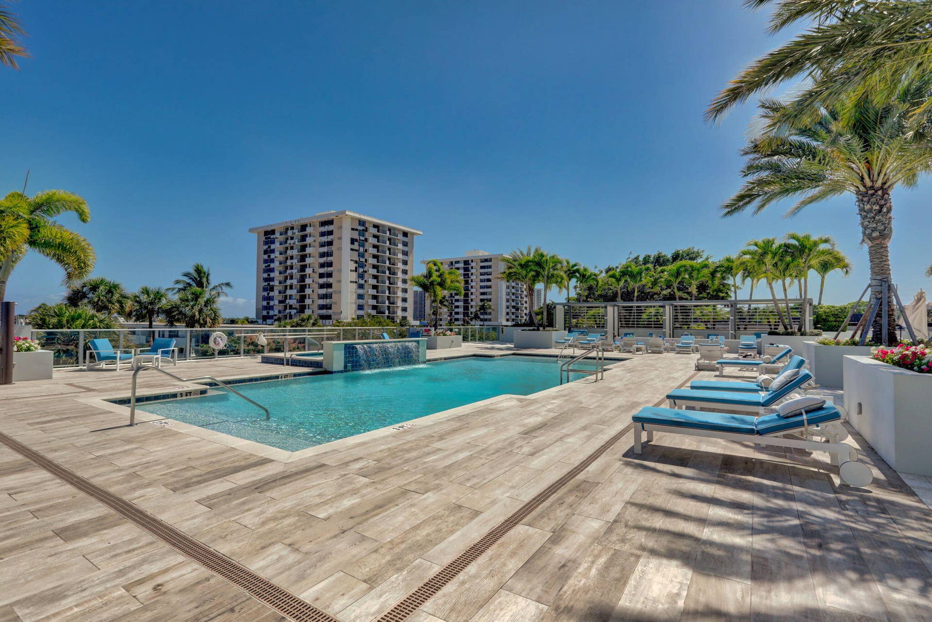 1 Water Club Way, #503, North Palm Beach, FL 33408 Swimming pool with an integrated waterfall feature, surrounded by a wood-finish deck and mature palm trees