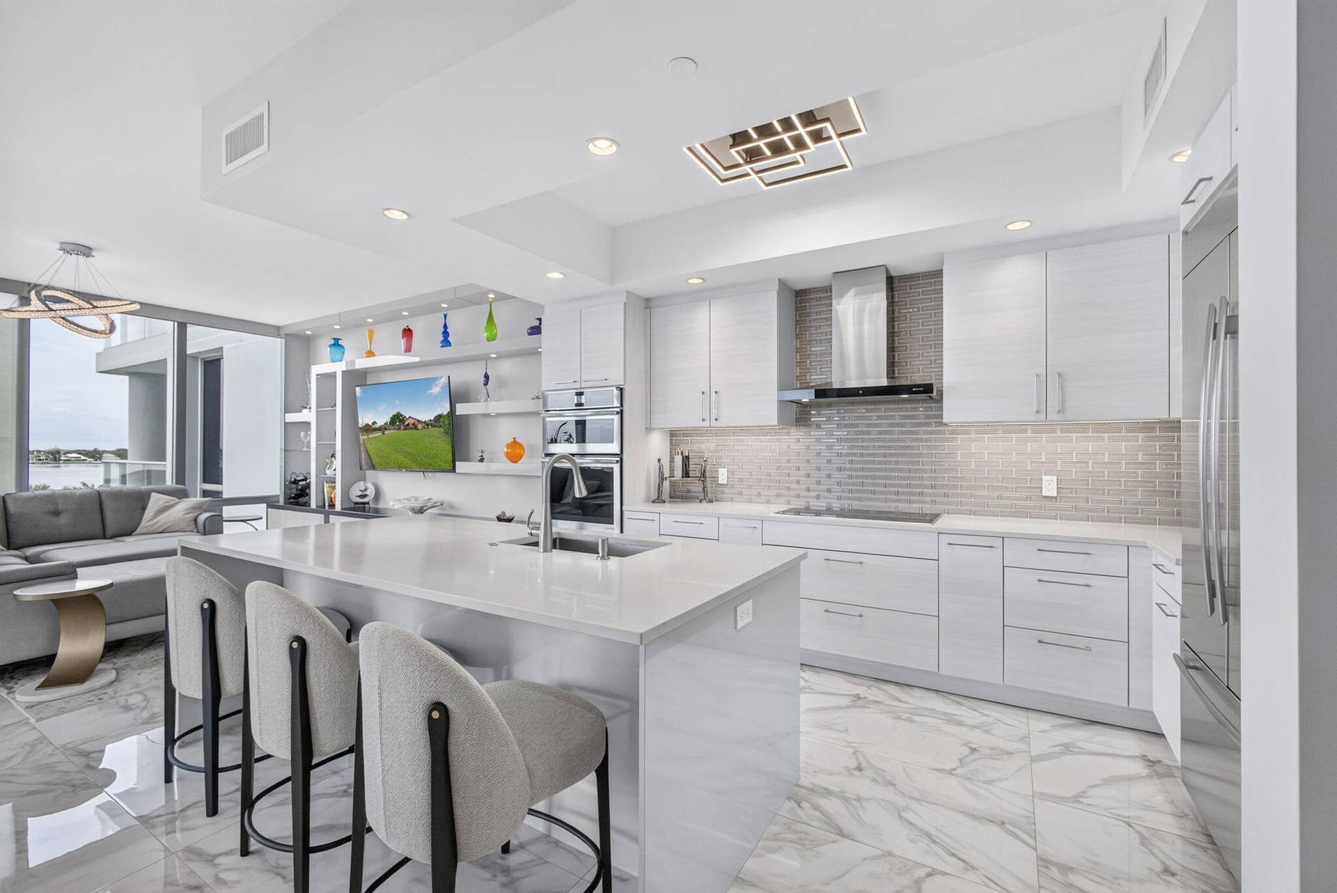 1 Water Club Way, #503, North Palm Beach, FL 33408 Spacious kitchen featuring an expansive island with seating, a sleek stainless steel range hood, built-in double ovens, and large format marble-look flooring