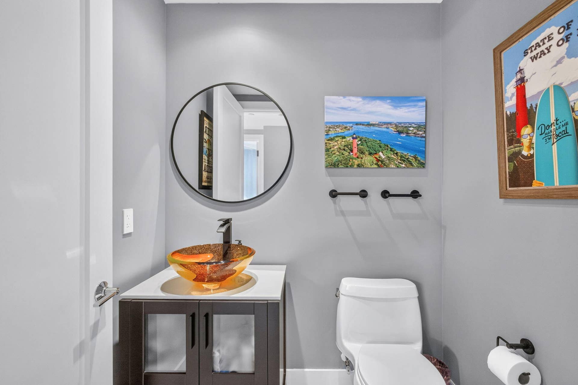 1 Water Club Way, #503, North Palm Beach, FL 33408 Wall-mounted circular mirror, vessel sink with dark faucet, dark wood-finish vanity with lower cabinetry, and white toilet