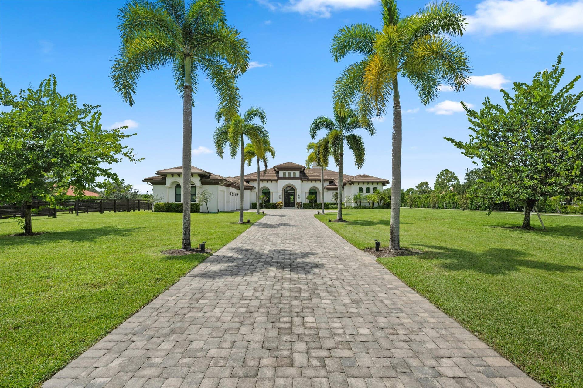 843 STALLION Drive, Loxahatchee, FL 33470 Paver driveway framed by mature palm trees, expansive green lawn, and a stucco exterior with arched windows