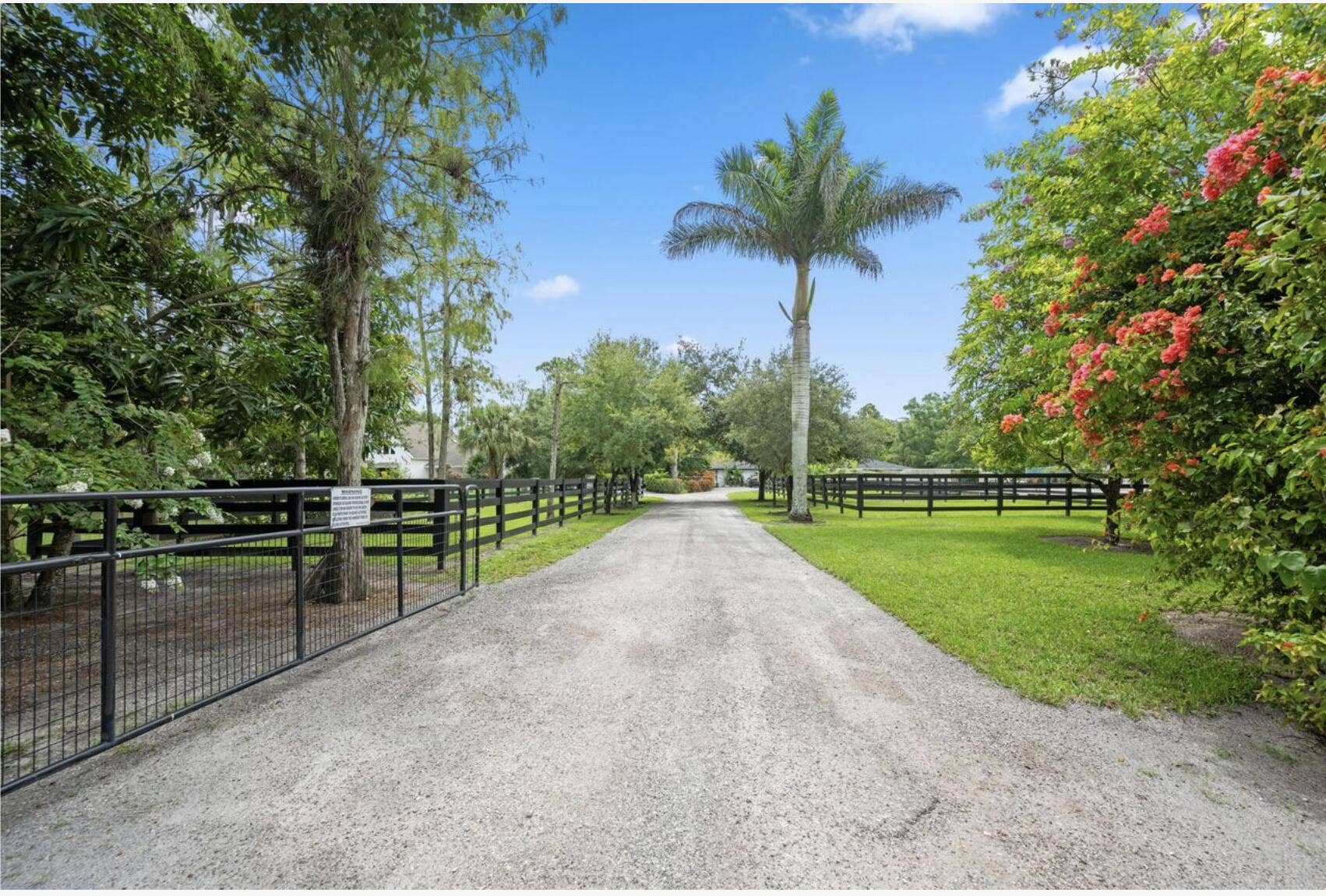 843 STALLION Drive, Loxahatchee, FL 33470 Gravel driveway for separate access to barn with black metal fencing, extensive green landscaping, and mature trees