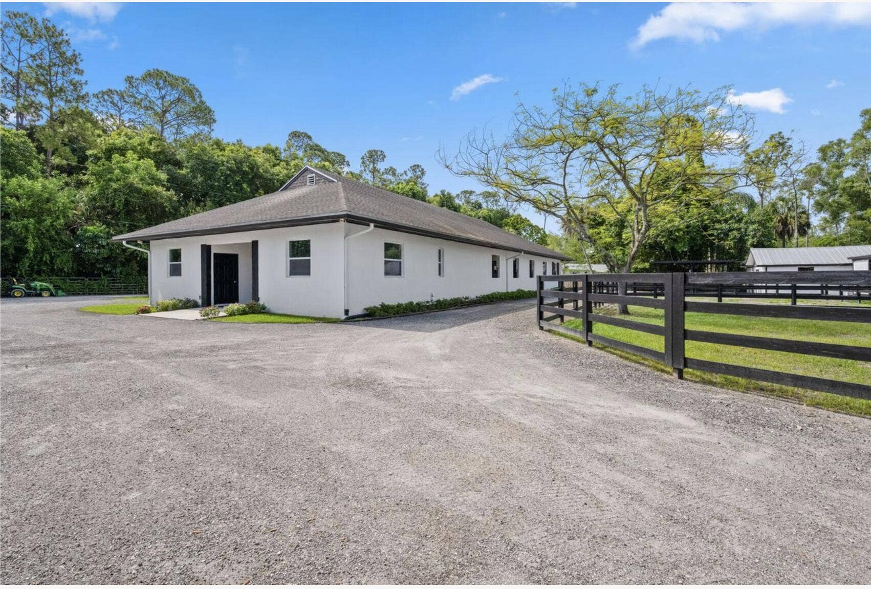 843 STALLION Drive, Loxahatchee, FL 33470 White stucco exterior with a dark shingle roof, complemented by a dark entry door and window frames