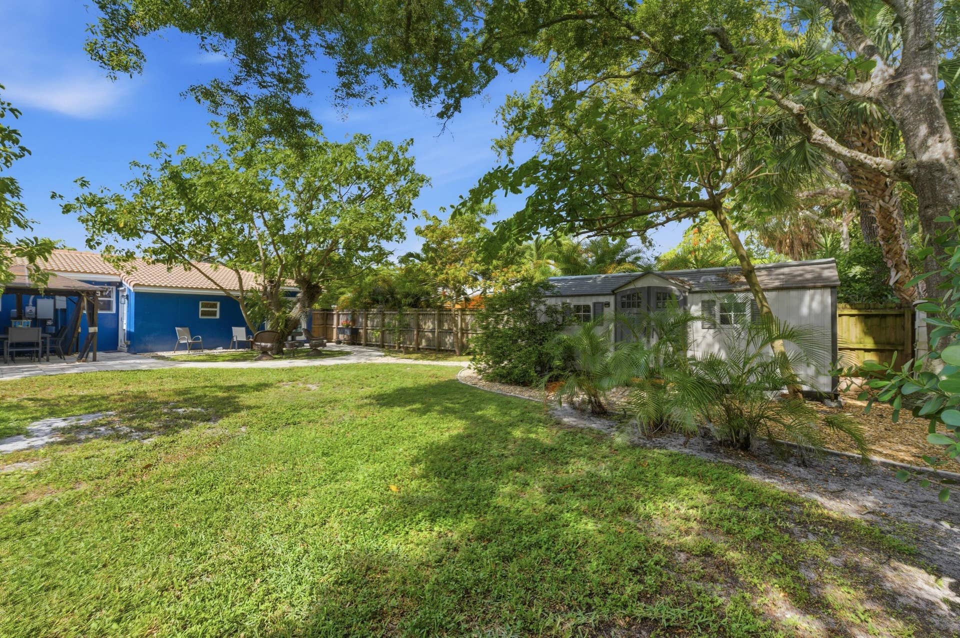1421 SW 20 Street, Fort Lauderdale, FL 33315 Expansive grassy yard with mature trees, a blue exterior structure, and a detached white storage shed with a shingle roof