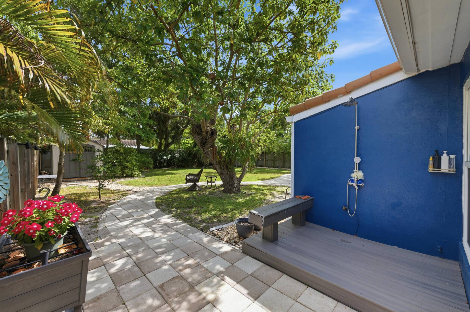1421 SW 20 Street, Fort Lauderdale, FL 33315 Paved pathway leading to a landscaped yard with mature trees, a composite deck, and an exterior shower fixture