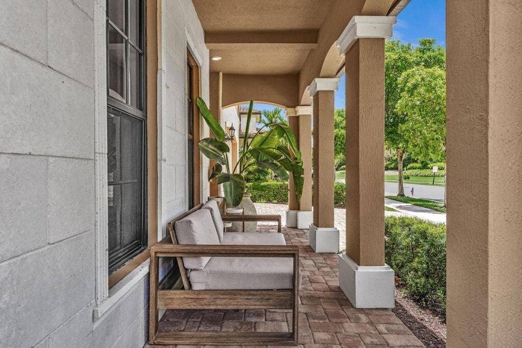 12143 S Baypoint Circle, Parkland, FL 33076 Covered front porch featuring a brick paver floor, stucco columns with white bases and caps, and a light-colored exterior wall with a dark-framed window