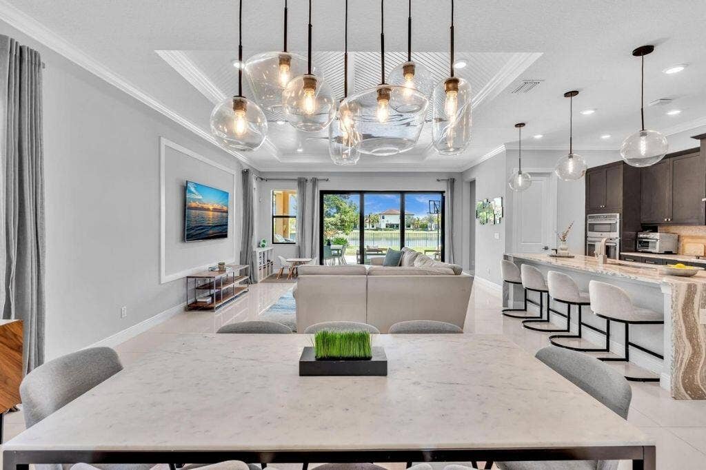 12143 S Baypoint Circle, Parkland, FL 33076 Spacious open-concept interior featuring light tile flooring, an ornate tray ceiling with contemporary pendant lighting, and a kitchen island with stone detailing