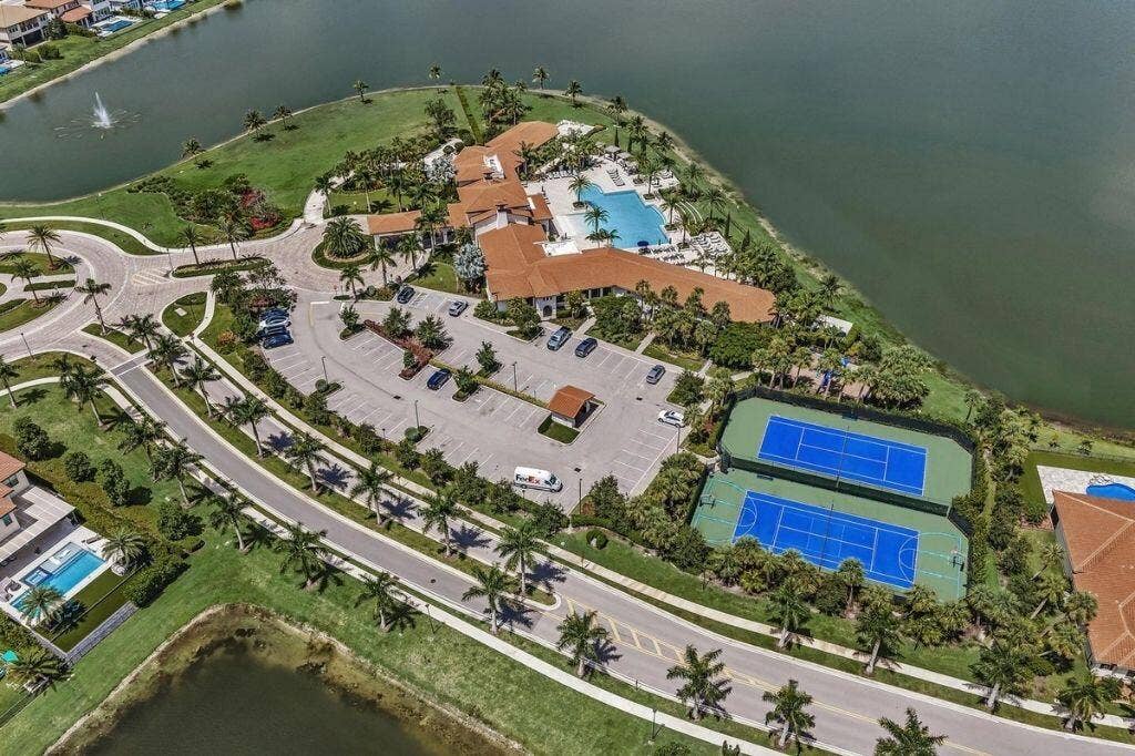 12143 S Baypoint Circle, Parkland, FL 33076 Extensive recreational facilities featuring two tennis courts, a large swimming pool, and a clubhouse with traditional tile roofing, all positioned alongside a substantial body of water