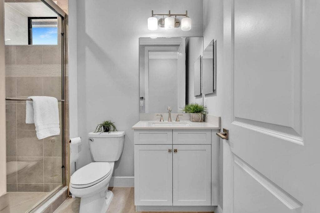 12143 S Baypoint Circle, Parkland, FL 33076 Bathroom featuring a glass-enclosed shower with tiled walls and a transom window, a white vanity with a countertop, a rectangular mirror, a three-light fixture, and wood-finish flooring