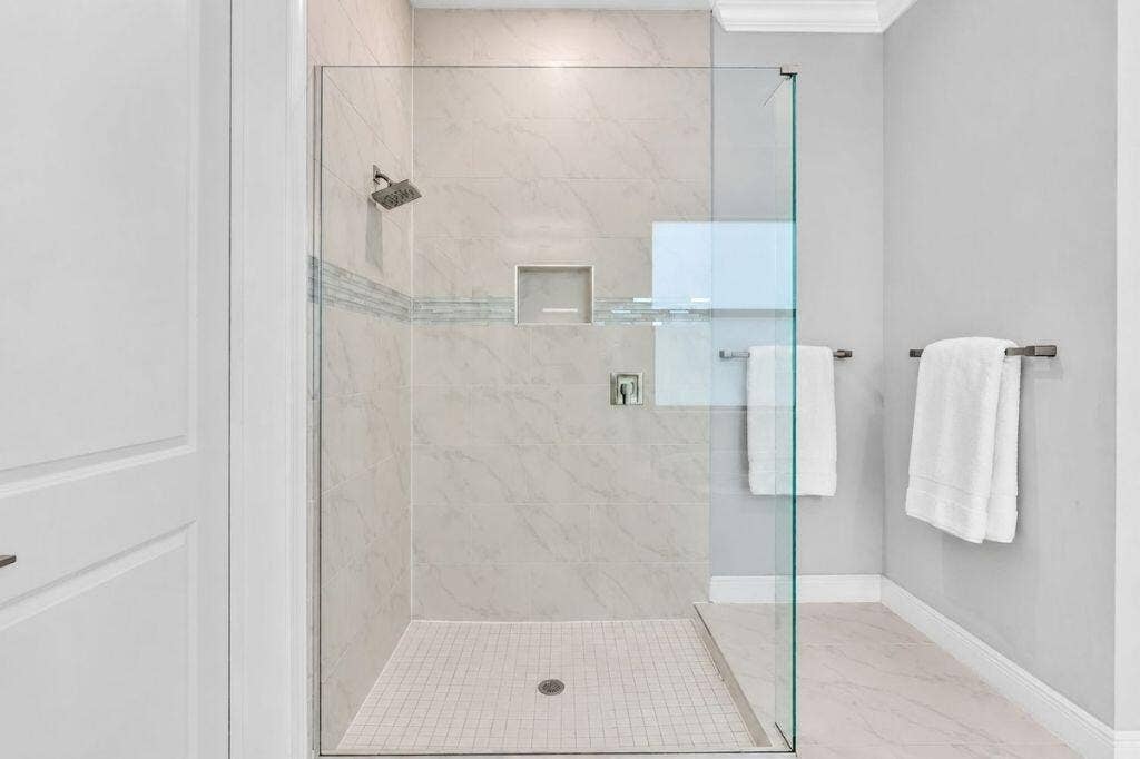 12143 S Baypoint Circle, Parkland, FL 33076 Glass-enclosed shower featuring large format wall tiles, a built-in niche, and a contrasting mosaic tile accent band
