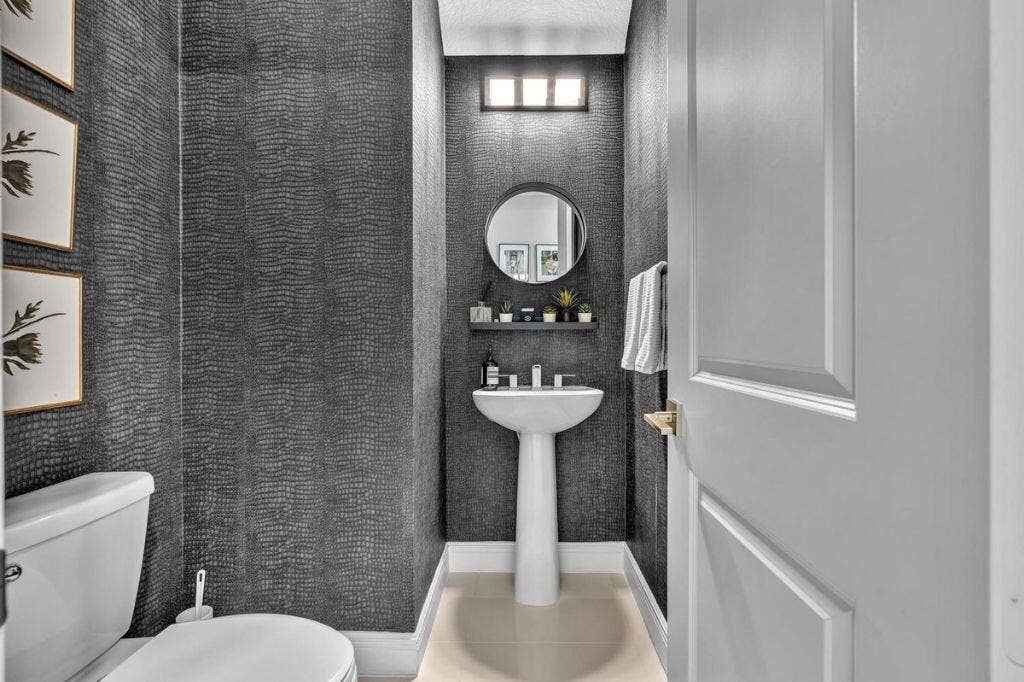 12143 S Baypoint Circle, Parkland, FL 33076 Powder room with textured dark gray wall covering, white pedestal sink, and a circular mirror