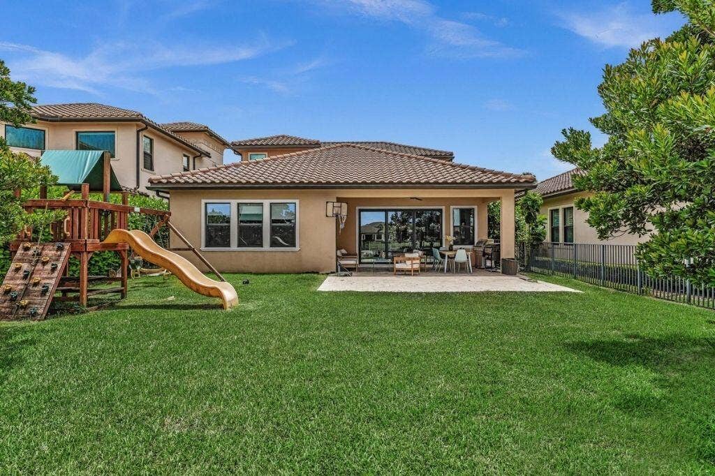 12143 S Baypoint Circle, Parkland, FL 33076 Expansive grassy yard featuring a covered patio, tiled roof, and stucco exterior