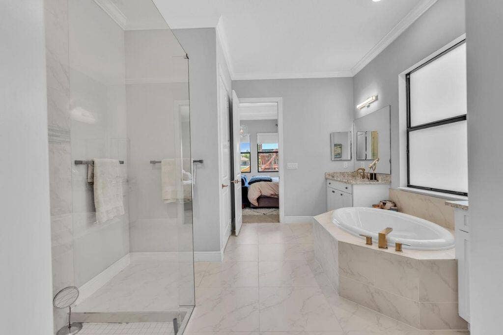 12143 S Baypoint Circle, Parkland, FL 33076 Spacious bathroom featuring a frameless glass shower enclosure, a built-in soaking tub with gold-tone fixtures, a vanity with a stone countertop, and tile flooring