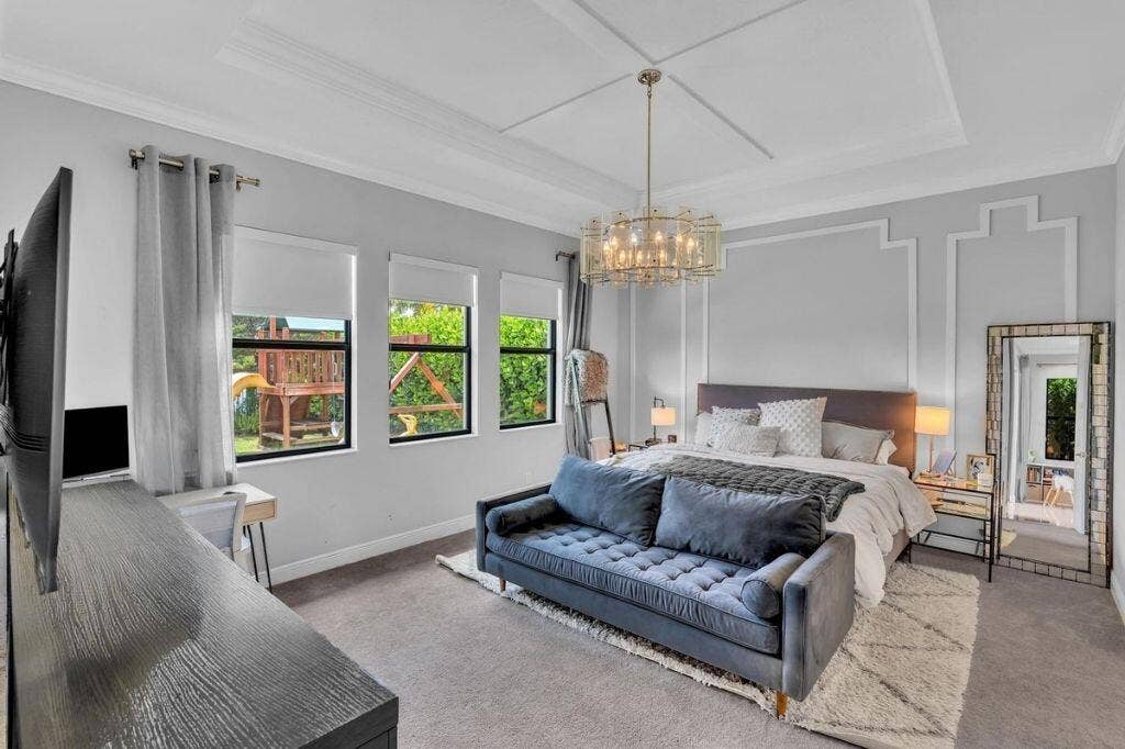 12143 S Baypoint Circle, Parkland, FL 33076 Spacious room featuring a tray ceiling with crown molding, a decorative chandelier, and three large windows