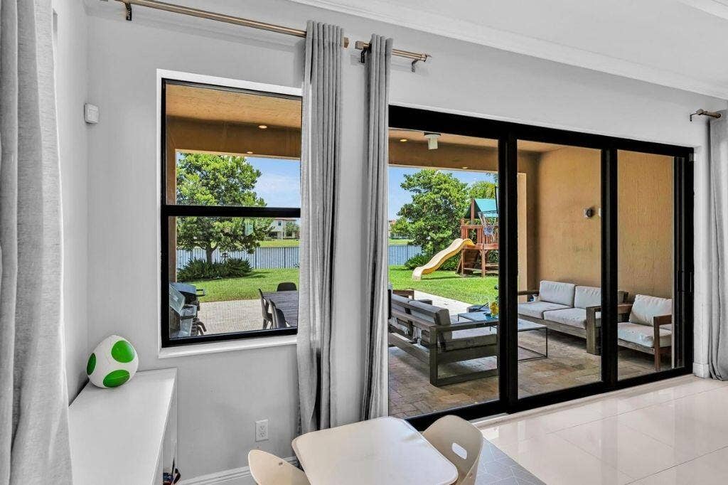 12143 S Baypoint Circle, Parkland, FL 33076 Stacable Sliding glass doors opening to a covered patio featuring a tiled surface and a grassy yard