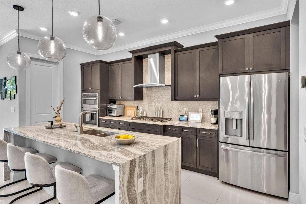 12143 S Baypoint Circle, Parkland, FL 33076 Gourmet kitchen featuring a waterfall island with stone countertop, stainless steel appliances, dark wood cabinetry, and recessed lighting