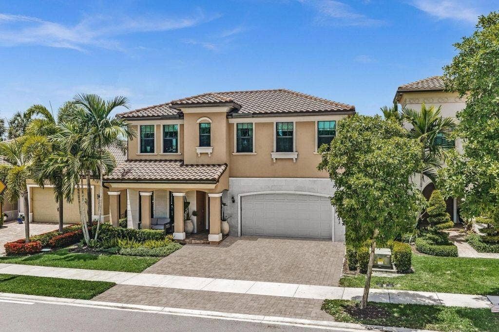 12143 S Baypoint Circle, Parkland, FL 33076 Mediterranean-style residence featuring a tile roof, stucco exterior, two-car garage, paver driveway, and mature palm trees