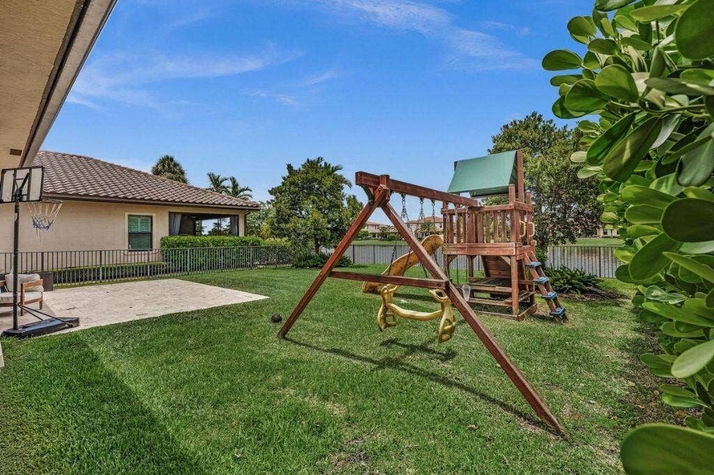 12143 S Baypoint Circle, Parkland, FL 33076 Expansive green lawn with a patio area, bordered by a privacy hedge and a metal fence
