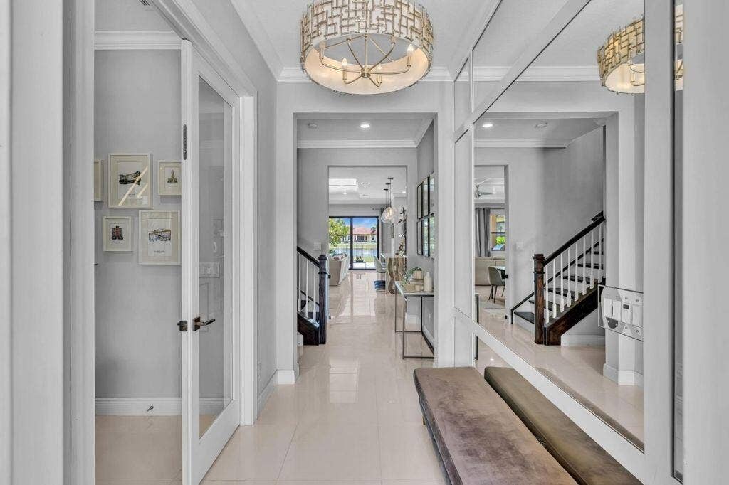 12143 S Baypoint Circle, Parkland, FL 33076 Grand entryway featuring a decorative ceiling fixture, tiled flooring, glass-paneled interior doors, and a dark wood-finish staircase with white risers