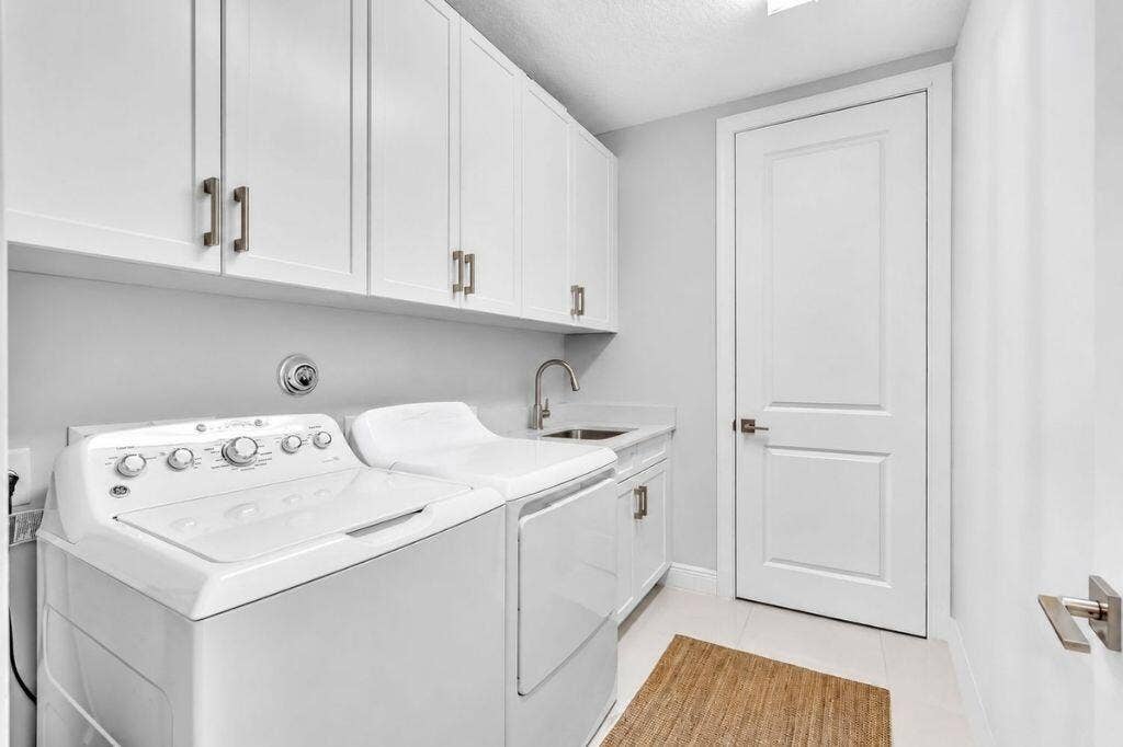 12143 S Baypoint Circle, Parkland, FL 33076 Dedicated laundry room featuring white cabinetry with brushed nickel hardware, a utility sink with a brushed nickel faucet, and light tile flooring