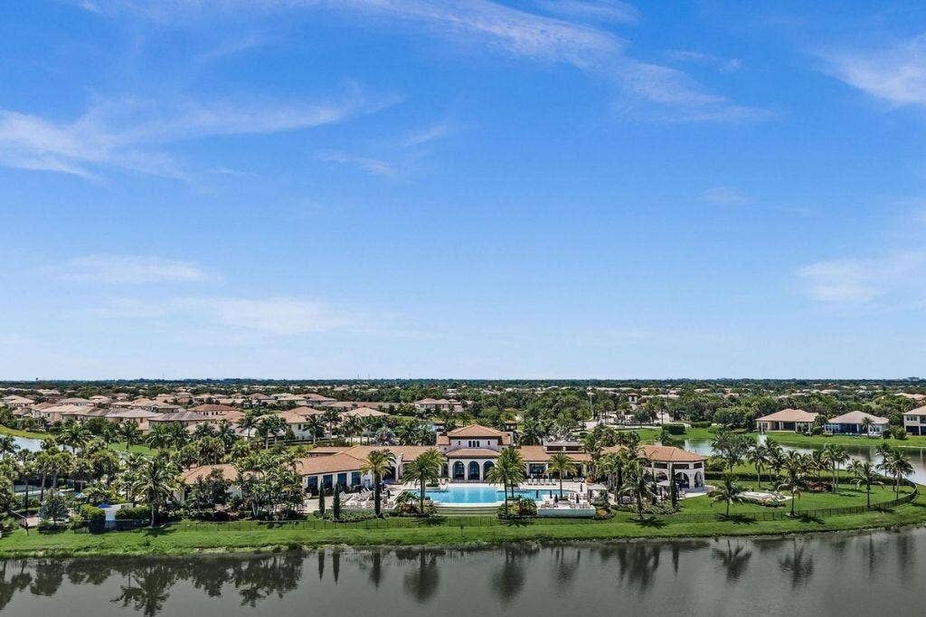 12143 S Baypoint Circle, Parkland, FL 33076 Lakeside property featuring a resort-style swimming pool with integrated spa, expansive paver decking, multiple covered lounge areas, and mature landscaping