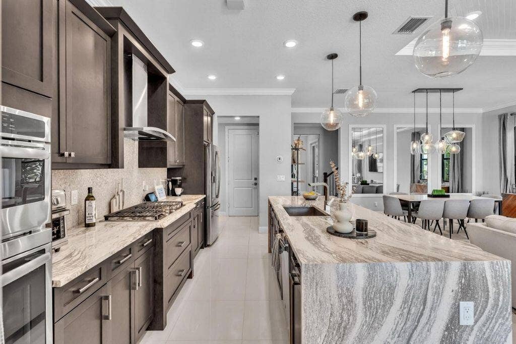 12143 S Baypoint Circle, Parkland, FL 33076 Gourmet kitchen featuring a waterfall island with integrated sink, stainless steel appliances, dark wood cabinetry, and recessed lighting