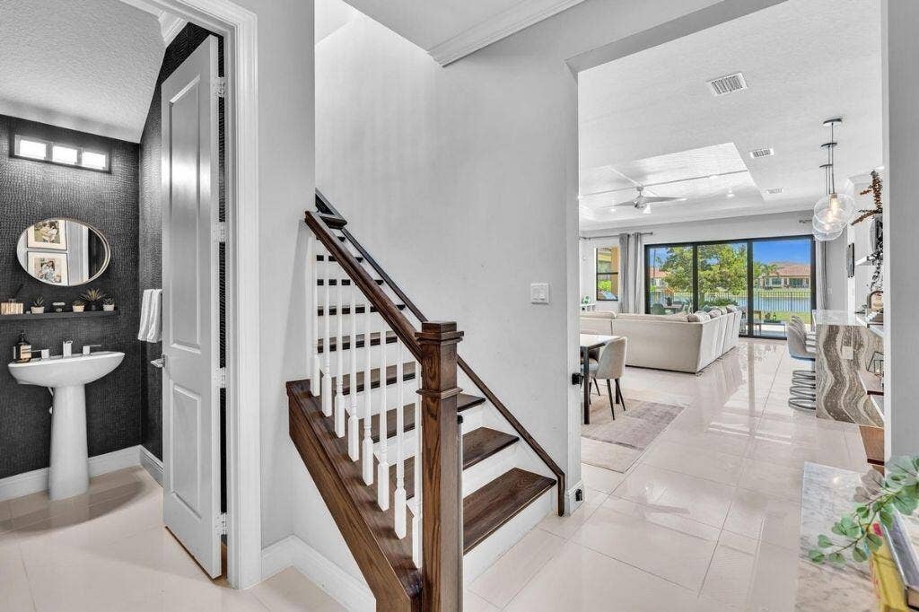 12143 S Baypoint Circle, Parkland, FL 33076 Hardwood staircase with white balusters, porcelain tile flooring, and a modern half-bath featuring a pedestal sink and dark textured wall covering