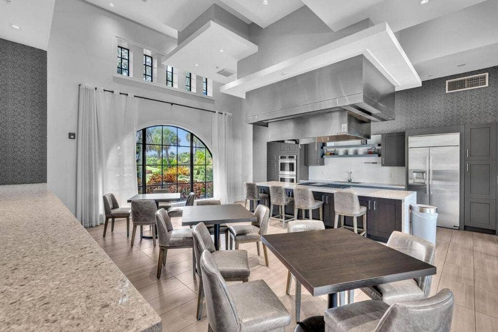 12143 S Baypoint Circle, Parkland, FL 33076 Spacious kitchen and dining area featuring a large arched window, vaulted ceilings, a substantial kitchen island with seating, a commercial-grade range hood, and integrated stainless steel appliances