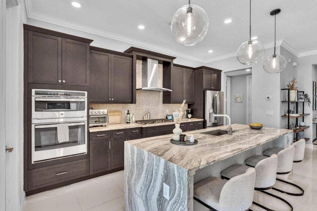 12143 S Baypoint Circle, Parkland, FL 33076 Gourmet kitchen featuring a waterfall island with integrated seating, dark wood cabinetry, stainless steel appliances, and pendant lighting