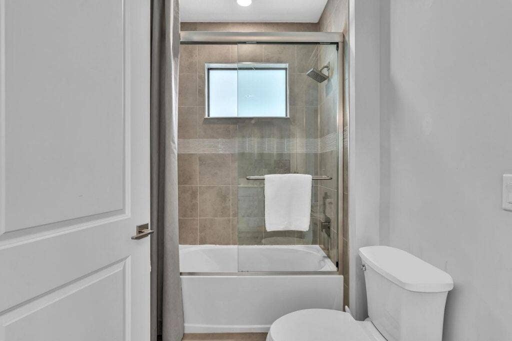 12143 S Baypoint Circle, Parkland, FL 33076 Bathroom featuring a white bathtub, glass shower enclosure, and tiled surround
