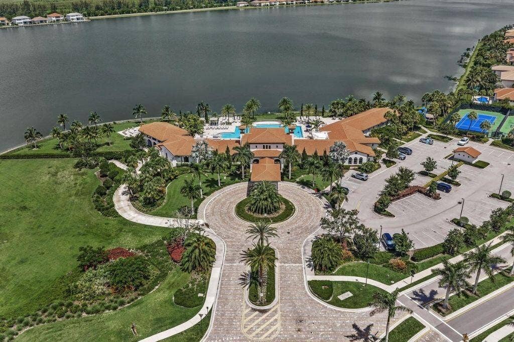 12143 S Baypoint Circle, Parkland, FL 33076 Expansive waterfront property featuring a large central building with a terracotta roof, multiple swimming pools, two tennis courts, and a circular paved driveway