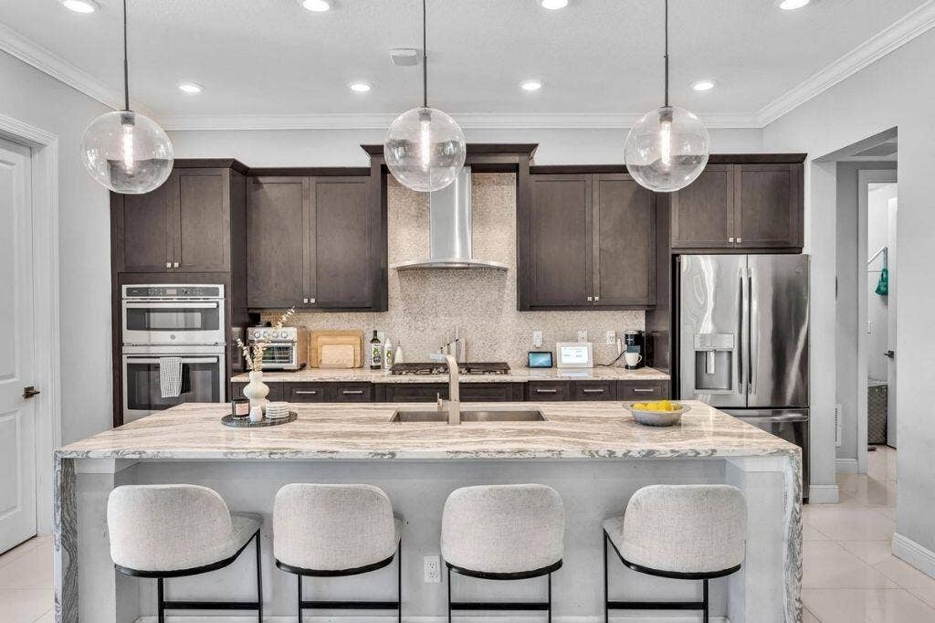 12143 S Baypoint Circle, Parkland, FL 33076 Kitchen featuring a large island with seating, stainless steel appliances, dark wood-finish cabinetry, a tile backsplash, and recessed lighting