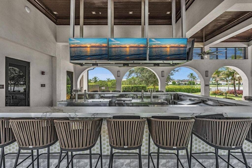 12143 S Baypoint Circle, Parkland, FL 33076 Outdoor bar area featuring a marble-look countertop, integrated stainless steel appliances, and multiple ceiling-mounted display screens