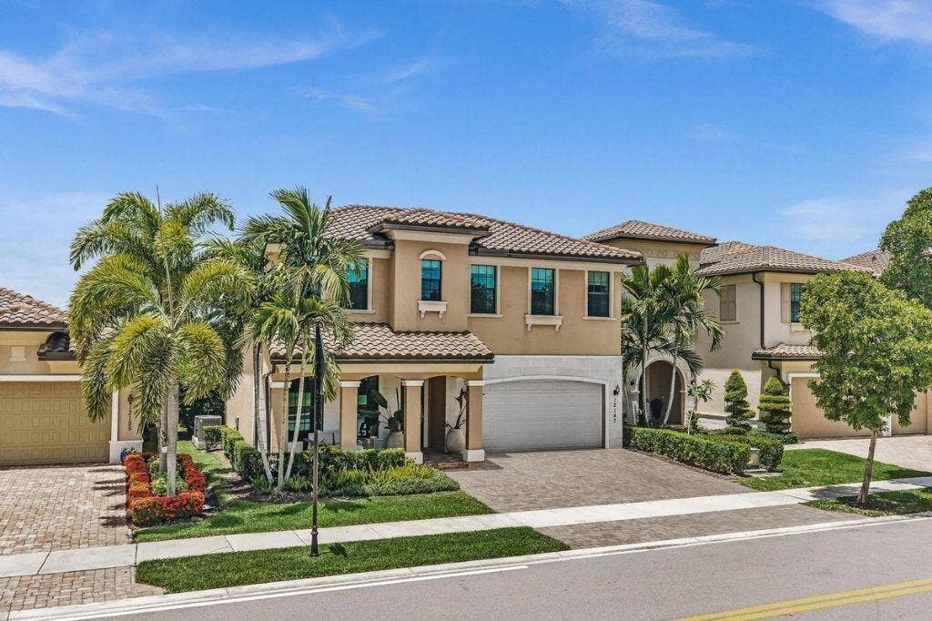 12143 S Baypoint Circle, Parkland, FL 33076 Mediterranean-style residence featuring a tile roof, stucco exterior, multiple arched windows, mature palm trees, and a paver driveway
