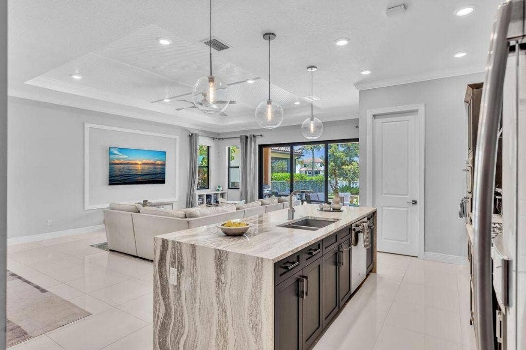 12143 S Baypoint Circle, Parkland, FL 33076 Open-concept kitchen featuring an expansive island with stone countertops, dark wood-finish cabinetry, and three pendant lights