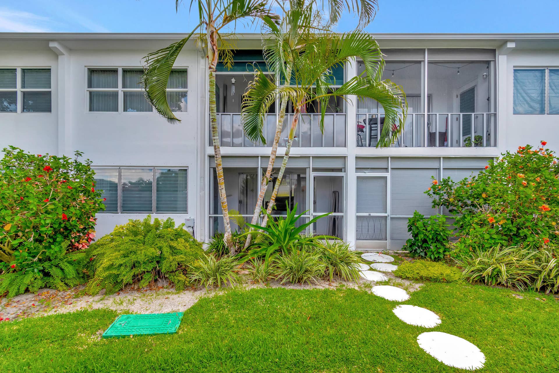 2161 NE 42nd Court, #116, Lighthouse Point, FL 33064 White stucco exterior with multiple windows, lush landscaping, a stone paver pathway, and two screened-in balconies