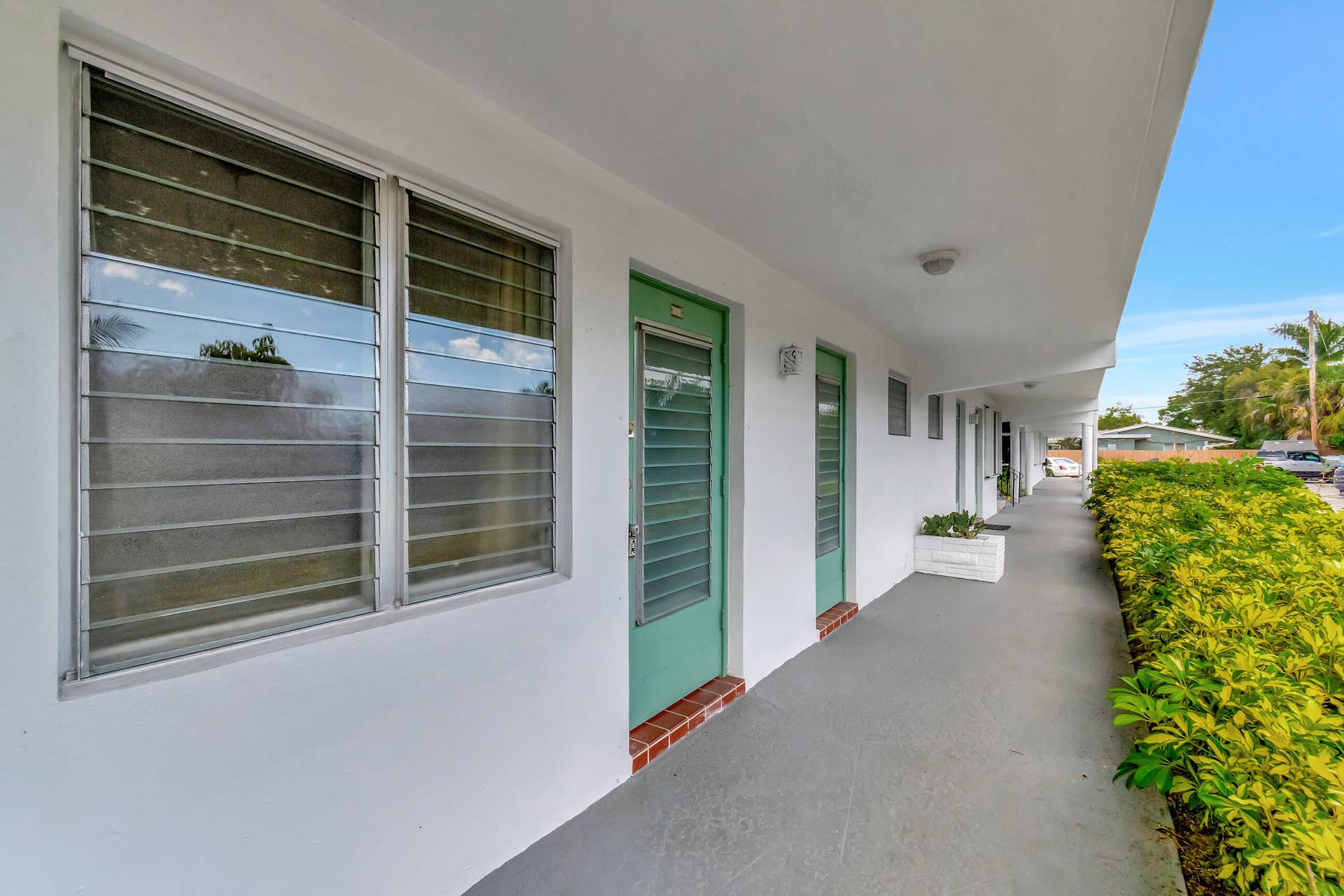 2161 NE 42nd Court, #116, Lighthouse Point, FL 33064 White exterior with green entry doors, louvered windows, and a paved walkway